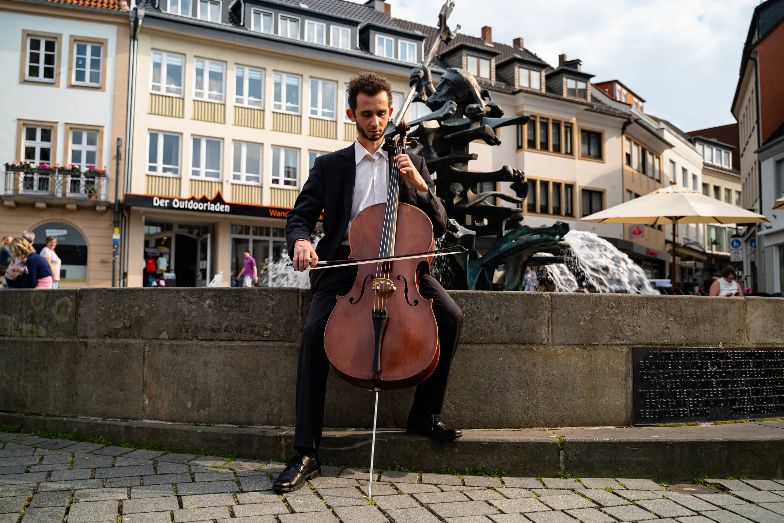 Ventsislav Harkov playing the cello by a fountain on a town square