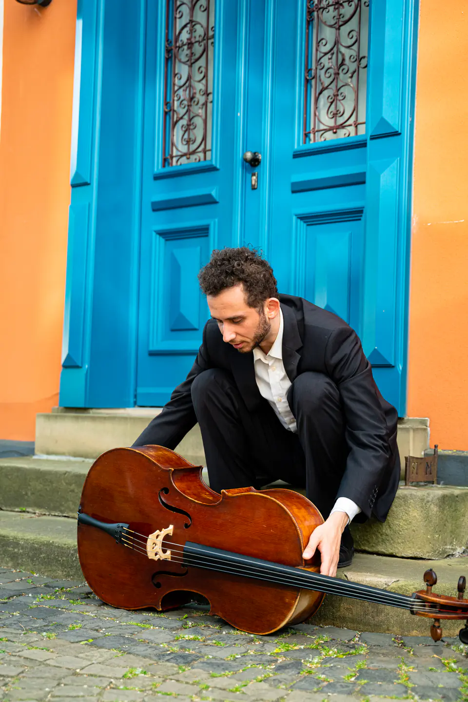 Ventsislav Harkov laying his cello down on the steps in front of a blue door