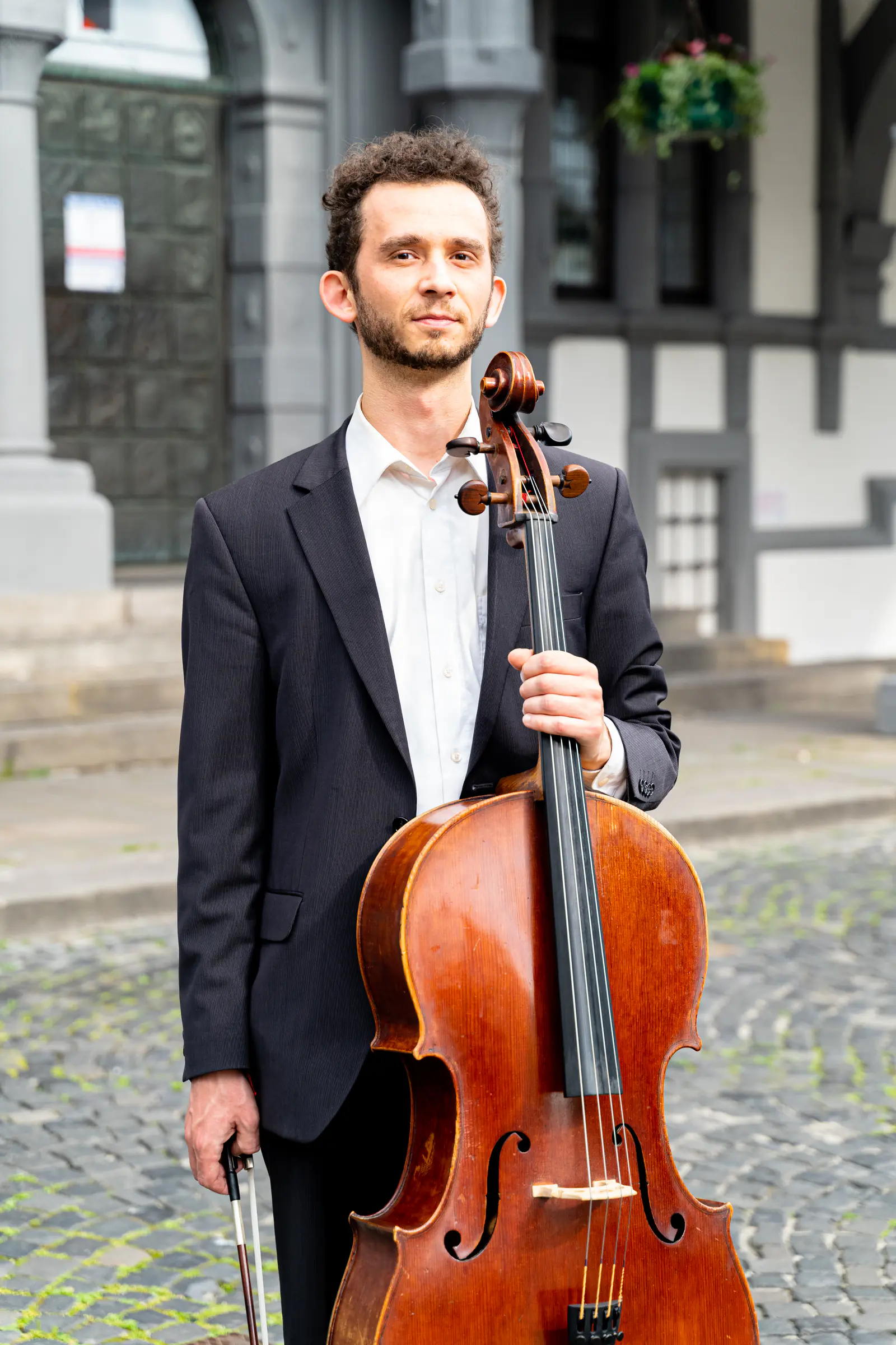 Ventsislav Harkov standing with his cello on a cobbled square in front of a historic building