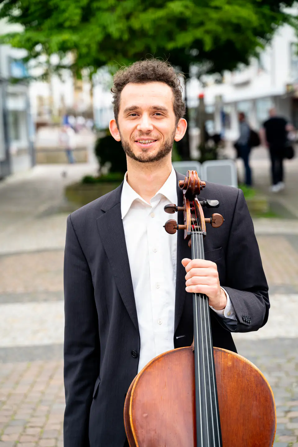 Portrait of a smiling Ventsislav Harkov with his cello in a pedestrian street