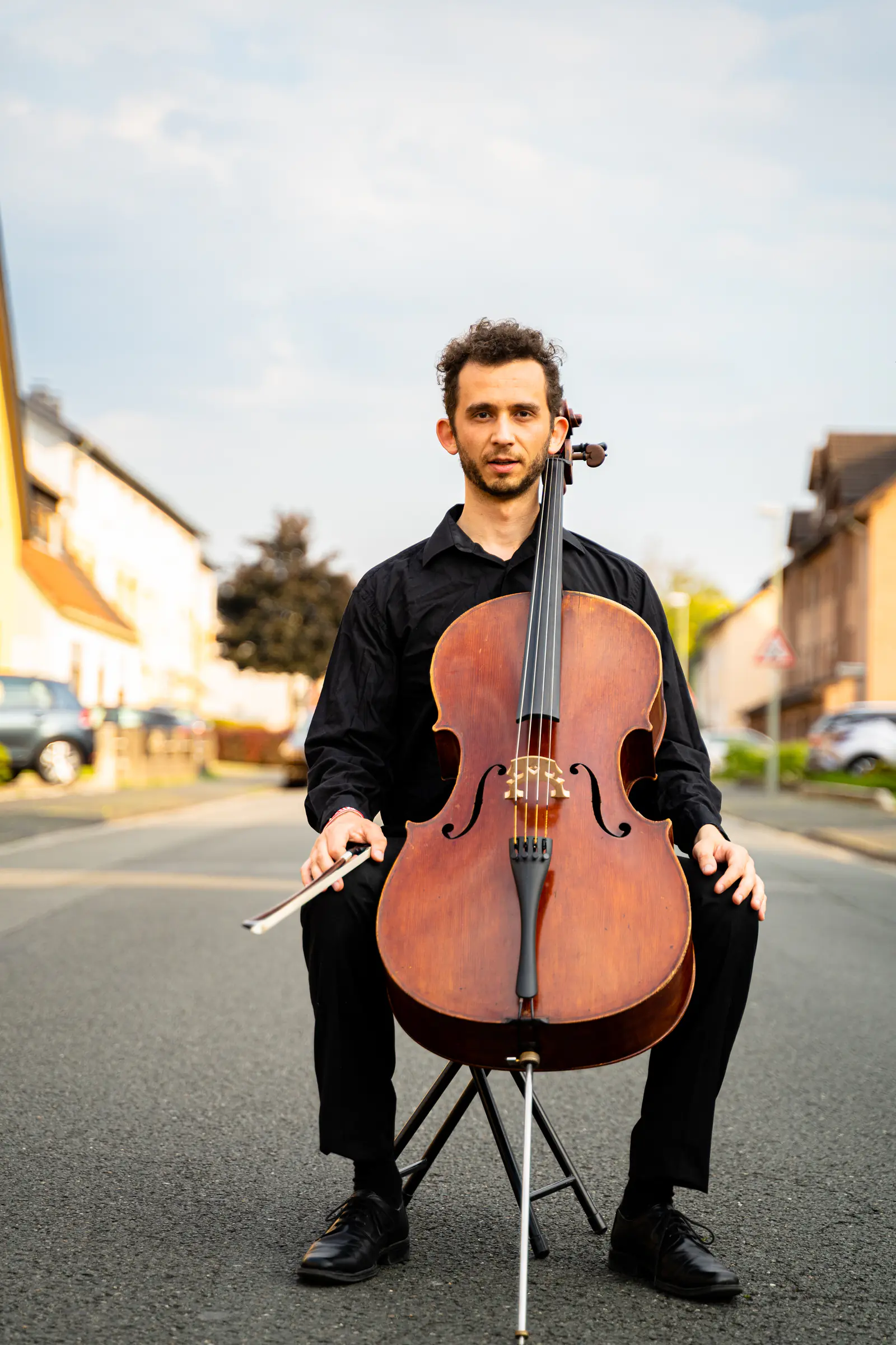 Ventsislav Harkov sitting with his cello in the middle of a quiet residential street